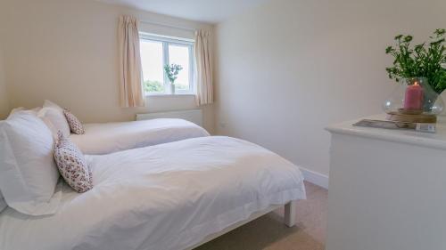 a white bedroom with two beds and a window at Gwyndy Bach in Trearddur