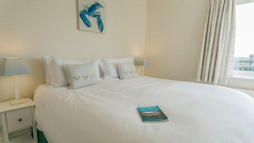 a bedroom with a white bed with a book on it at Gwyndy Bach in Trearddur