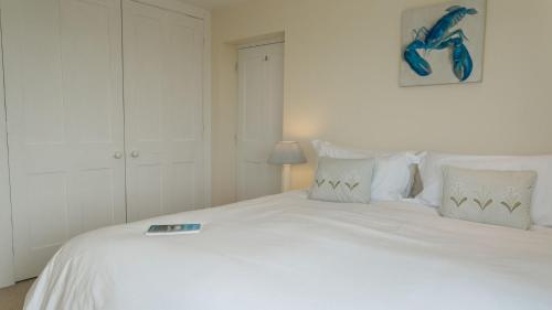 a white bed with white pillows and a picture on the wall at Gwyndy Bach in Trearddur