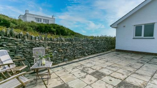 a patio with two chairs and a stone wall at Gwyndy Bach in Trearddur
