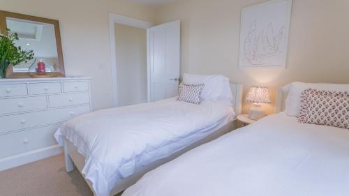a white bedroom with two beds and a dresser at Gwyndy Bach in Trearddur