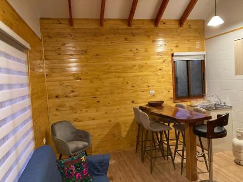 Habitación con pared de madera, mesa y sillas. en Cabañas Alto Quillay, radal siete tasas, en El Torreón