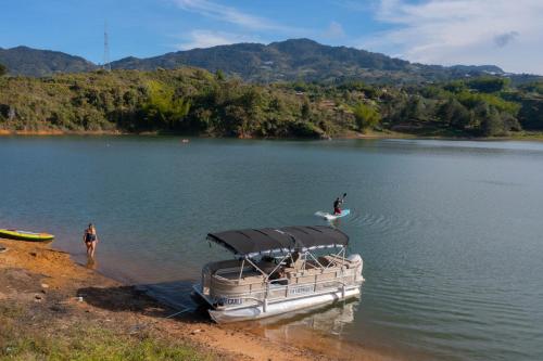 a boat on a lake with a person on a surfboard at Glamping Montecarlo Lodge Cubo de Madera-Guatapé in Guatapé