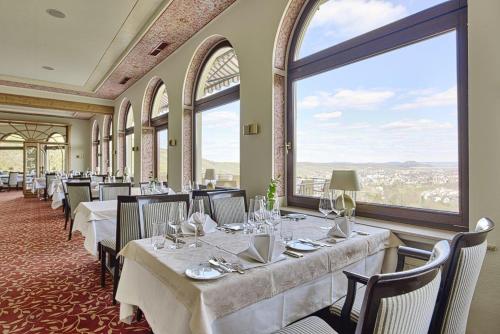 un ristorante con tavoli e sedie bianchi e ampie finestre di Hohenzollern a Bad Neuenahr-Ahrweiler