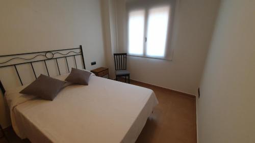 1 dormitorio con 1 cama blanca, ventana y silla en La Yecla Teruel, en Teruel