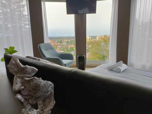 a bedroom with a bed and a chair and a large window at WEST Panorama Penthouse - apartment with a fantastic view of the city in Szombathely