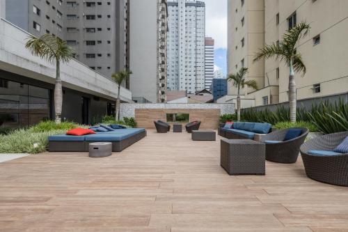 a patio with couches and chairs and palm trees at Helbor Stay Batel in Curitiba