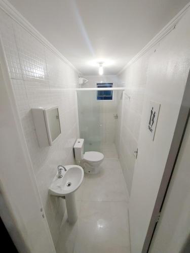 a white bathroom with a toilet and a sink at Ap frente para o mar in Caraguatatuba