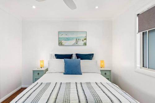 Dormitorio blanco con cama con almohadas azules en Rothery Escape - A Cosy Coastal Cottage en Bellambi