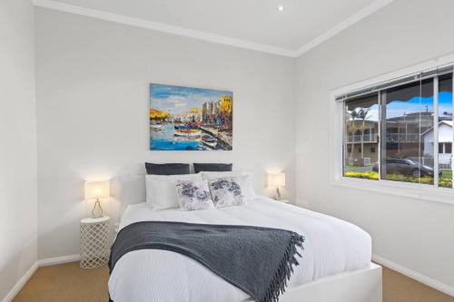 a white bedroom with a large bed and a window at Saltwater Escape - Live the Sand and Surf Lifestyle in Thirroul