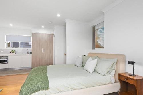a white bedroom with a bed and a kitchen at Rockpool Escape - A Coastal Refresh near the Marina in Shellharbour