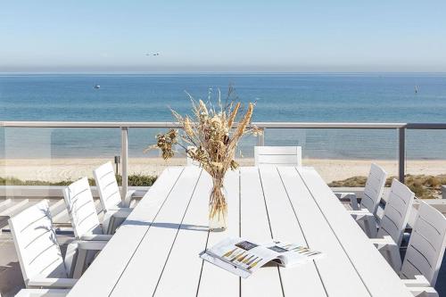 a white table with white chairs and the beach at Bonbeach Bliss - Contemporary Waterfront Living in Melbourne