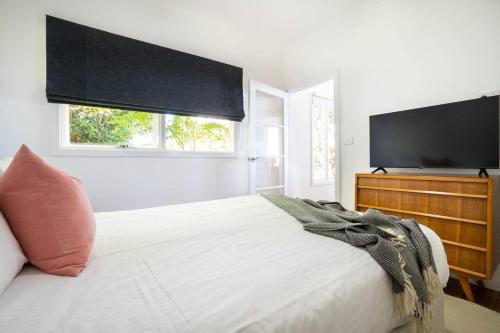 a white bedroom with a large bed with a flat screen tv at Couples Corner - A Stylish Bay View Retreat in McCrae