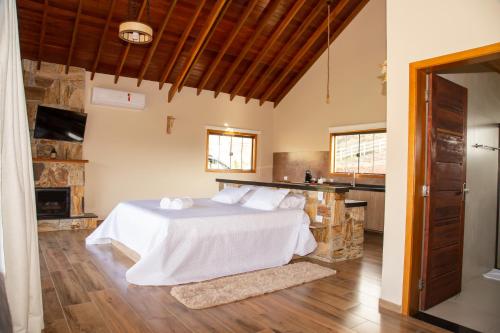 a bedroom with a white bed and a kitchen at Chalé Pedra Madeira in São Bento do Sapucaí