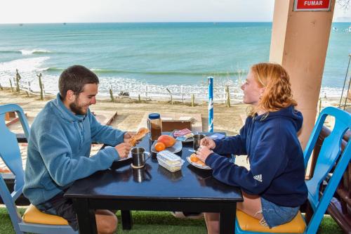 Ein Mann und eine Frau sitzen an einem Tisch am Strand in der Unterkunft La Casona de Lobitos - Cowork in Lobitos