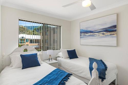 a white bedroom with two beds and a window at Esplanade Escape - Beachfront Family Bliss in Thirroul