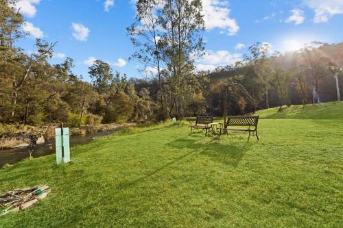 two benches sitting in the grass next to a river at Parsons Flat River Barn in Dargo