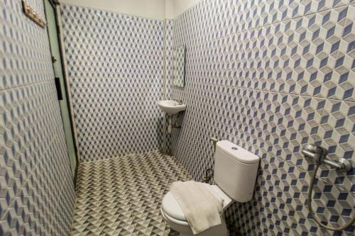 a bathroom with a toilet and a tiled wall at Bwalk Hotel Malang in Sengkaling