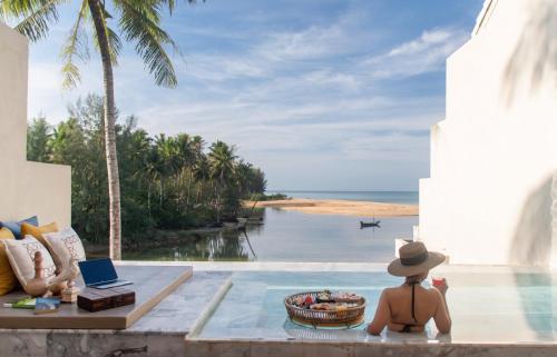 a man in a hat sitting in a pool looking out at the ocean at Devasom Khao Lak Beach Resort & Villas in Khao Lak