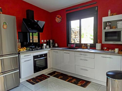 a kitchen with white cabinets and a red wall at Le Coin Zen in Ravine des Cabris