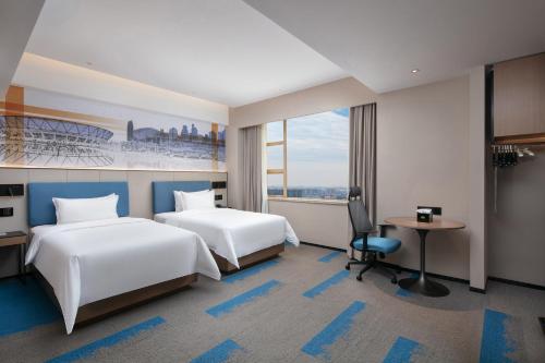a hotel room with two beds and a desk at Hampton by Hilton Foshan Dali in Foshan