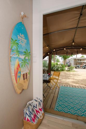 une planche de surf suspendue sur un mur à côté d'une terrasse couverte dans l'établissement Camping Les Jardins d Agathe, au Grau-dʼAgde