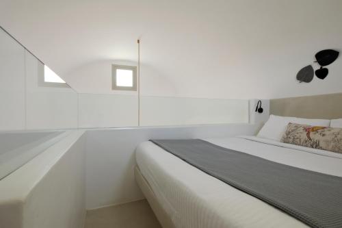 a white bedroom with a bed and a window at Adorno Oia in Oia
