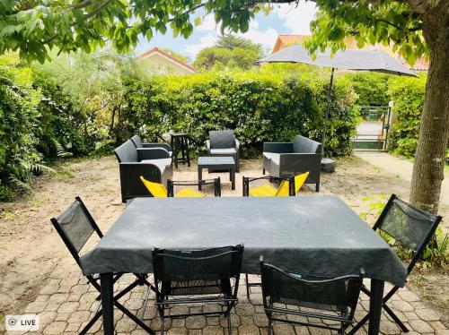 a table with chairs and an umbrella in a yard at Mimizan Surf & Beach House 250m océan + forêt in Mimizan