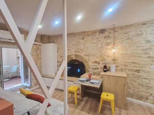 een woonkamer met een stenen muur, een tafel en gele krukken bij Studio plein centre-ville 2 in Nîmes