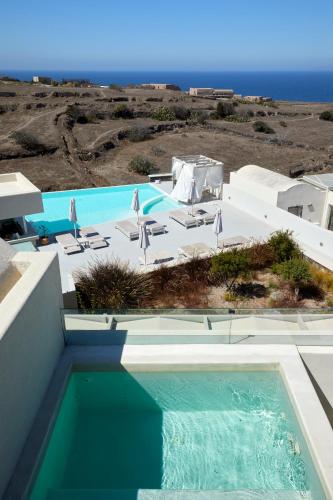 a swimming pool with chairs and the ocean in the background at Adorno Oia in Oia