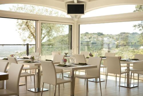a restaurant with white tables and chairs and large windows at Al Mirador Resort in Selva di Fasano