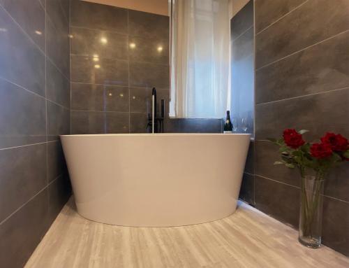 baño con bañera blanca y jarrón de rosas rojas en Casa Rosmini rooms, Dolomia best home, en Trento