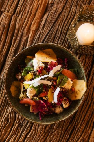 a bowl of salad on a wooden table with a candle at Caravan AlUla by Our Habitas in AlUla