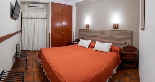a bedroom with a bed with an orange bedspread at Hotel Los Sauces in Cafayate
