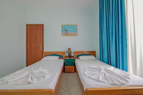 two beds in a room with blue curtains at Hotel Divo Palace in Ksamil