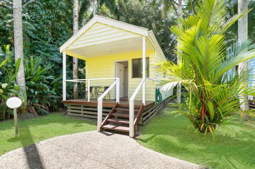 a small yellow house with a wooden porch in a yard at Mossman Resort Holiday Villas in Mossman