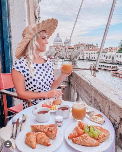 a woman in a hat sitting at a table with food at Palazzetto Pisani Grand Canal in Venice