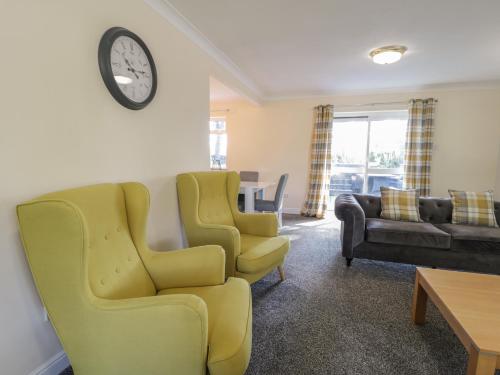 a living room with yellow chairs and a clock on the wall at Woodlands Retreat in Ruthin