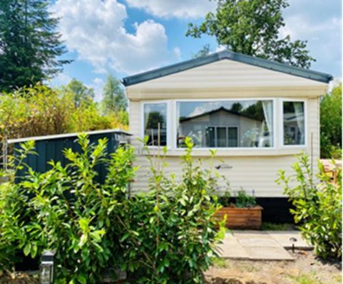 a small white house with a window in a garden at Nessy's Place (sta caravan) in Oude Willem