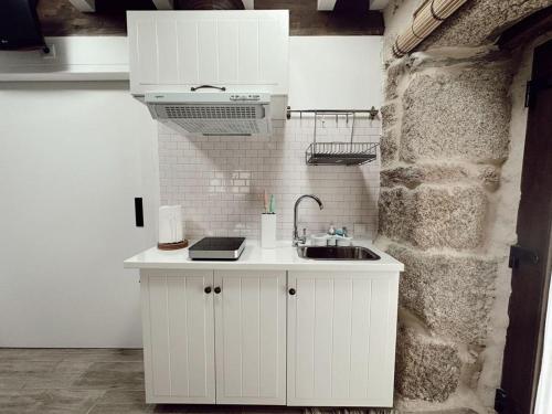 uma cozinha branca com um lavatório e uma parede de pedra em A XANELA 