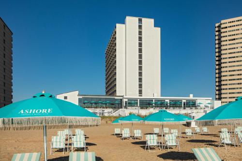 a beach with chairs and umbrellas in front of a building at Ashore Resort & Beach Club in Ocean City