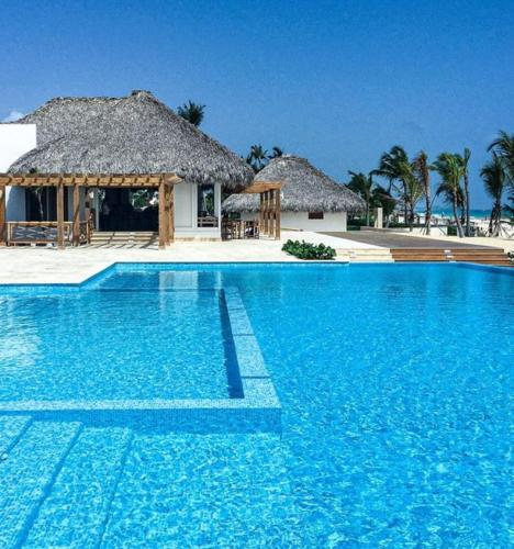 a large blue swimming pool with a thatched building at Hard Rock at Cana Pearl 1 by Unwind Properties in Punta Cana