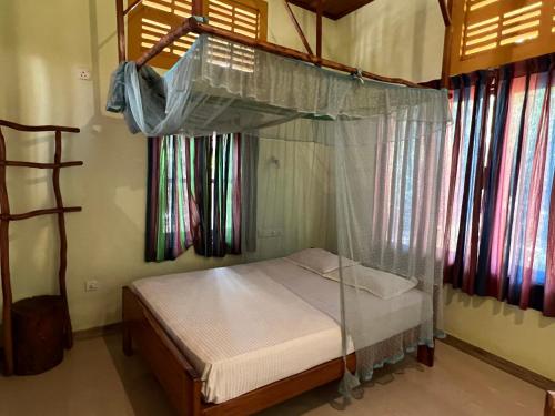 Bett mit Baldachin in einem Zimmer mit Fenstern in der Unterkunft Kirushna in Arugam Bay