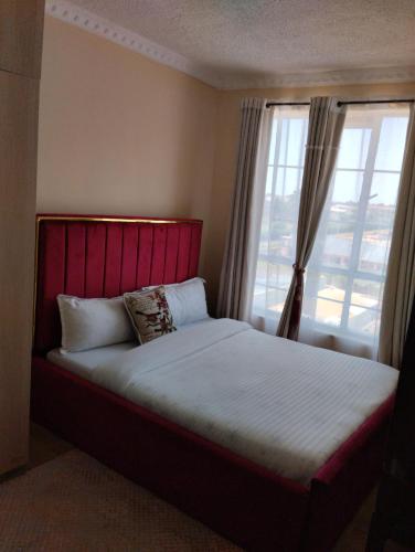 um quarto com uma cama com uma cabeceira vermelha e uma janela em TajHomes em Eldoret