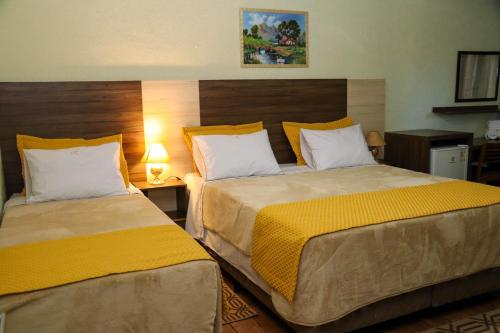 a hotel room with two beds with yellow and white pillows at HOTEL ESTÂNCIA - ESTACIONAMENTO GRATUITO ROTATIVO - Vagas Limitadas in Poços de Caldas