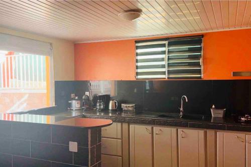 a kitchen with orange and black cabinets and a sink at Appartement charmant à Les Abymes avec piscine privée, 60m² in Les Abymes