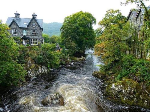 a river in a town with houses and trees at Cosy Cottage, Nr Betws y Coed. in Llanrwst