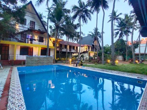 a swimming pool in front of a house with palm trees at PV Cottages Serenity Beach in Puducherry