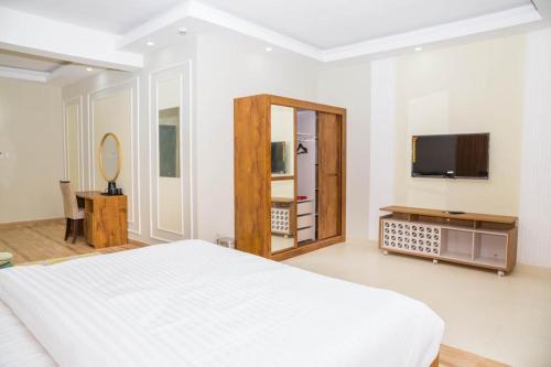 a white bedroom with a bed and a tv at Itten Plaza Hotel 2 in Salalah