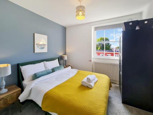 a bedroom with a bed with a yellow blanket and a window at Margaret's Loft in Cheltenham